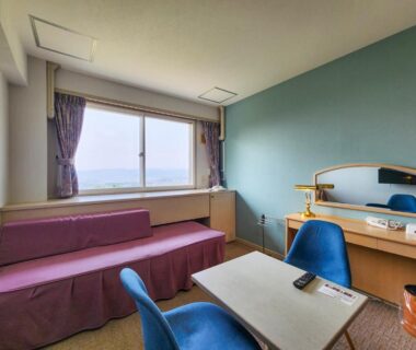 Guest room with seating area, desk, mirror and large window at Iwanai Kogen Hotel, Hokkaidō