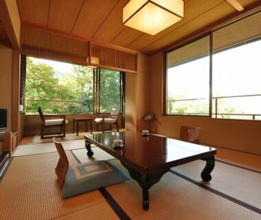 Tatami room with low wooden table, floor cushions and large windows overlooking trees at Iwaso in Hiroshima
