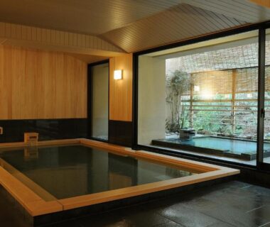 Indoor wooden onsen bath with large window overlooking courtyard garden at Iwaso in Hiroshima