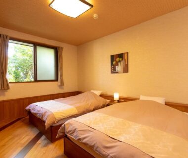 Two single beds, wooden flooring and curtained window with greenery at Iyashi no Yado Iroha in Ōita, Kyūshū, Japan