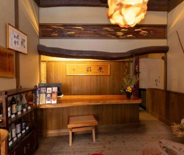 Traditional wooden reception counter with hanging lantern and sake display at Iyashi no Yado Iroha Ōita Kyūshū