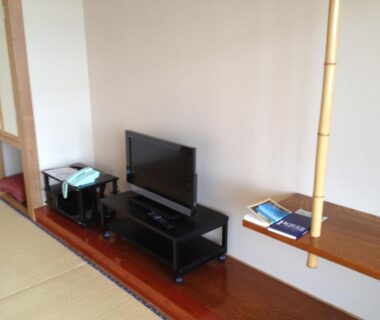 Tatami-floored room with low TV stand, kettle and wooden shelf at Iyashinoyado Rodem Iwate