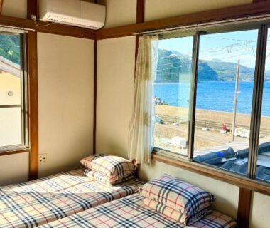 Tatami room with twin futons and large window overlooking the coastline in Izu Hokkawa, Shizuoka