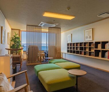 Calm ryokan lounge with wooden chairs, green ottomans and bookshelf by window slats