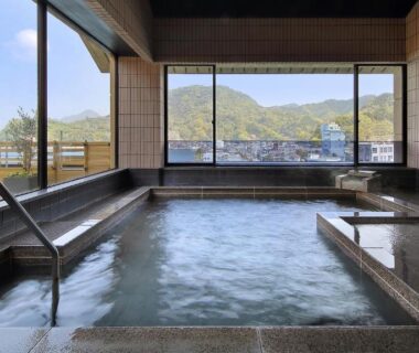 Indoor communal onsen bath with tiled floor and large windows overlooking mountains and town in Shizuoka