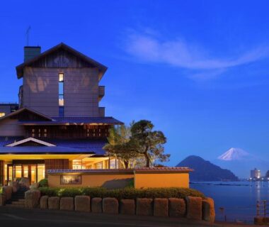 Evening view of Izu Mitohama Shotokan by calm coastal waters with distant mountains and harbor boats in Shizuoka