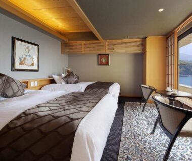 Twin beds with low chairs by large window overlooking coastal waters at Izu Mitohama Shotokan, Shizuoka