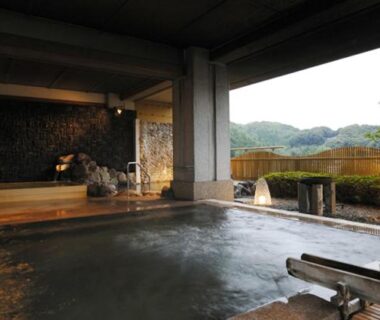 Sheltered onsen bath with stone and wooden accents and distant mountain backdrop at Izu-Nagaoka Hotel Tenbo, Shizuoka