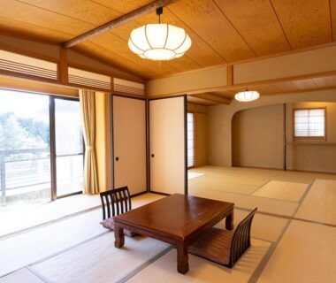 Sunlit tatami room with low wooden table, floor chairs, sliding doors and balcony access at Izu Nagaoka Kinjokan, Shizuoka, Japan