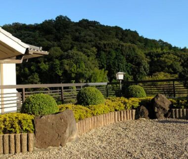 Gravel courtyard with clipped shrubs, stone accents and hillside backdrop at Izu Nagaoka Kinjokan, Shizuoka