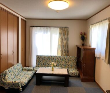 Sitting area with low table, patterned sofas, wooden closets and curtained windows at Izu Shirada Villa in Shizuoka