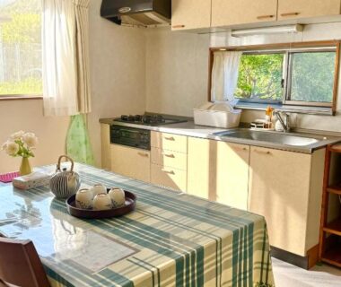 Sunlit kitchenette with table, checkered tablecloth, teapot and chairs at Izu Shirada Villa, Shizuoka