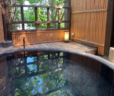Circular tiled wooden bath with bamboo fence and trees at Izu Atagawa Yubana Mankai, Shizuoka