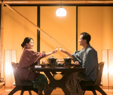 Couple in traditional robes clinking glasses across low table in tatami room at Izu Atagawa Yubana Mankai, Shizuoka