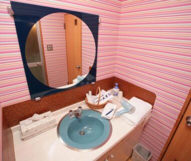 Round mirror and blue sink on striped pink vanity counter with toiletries at Izuito Onsen Daitokan Shizuoka