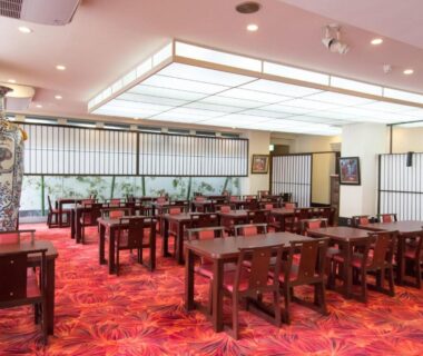 Spacious ryokan dining room with wooden tables, shoji screens and red patterned carpet at Izuito Onsen Daitokan in Shizuoka