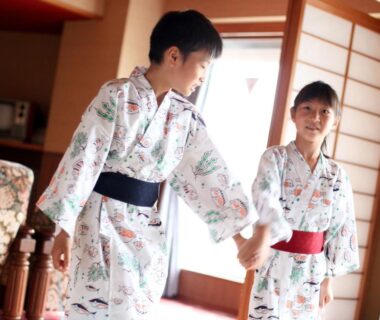 Two children in patterned yukata holding hands in a ryokan room with shoji screens at Izuito Onsen Daitokan, Shizuoka, Chūbu