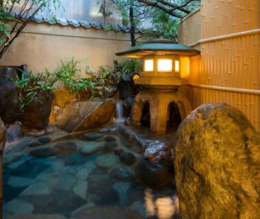 Stone-lined outdoor onsen with lantern, bamboo fence and rock features at Izumi-so in Gifu, Chūbu