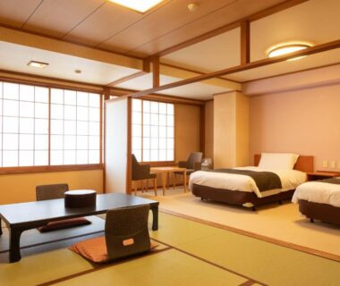 Tatami seating area with low table and twin beds at Izumiso ryokan in Nagano, Chūbu