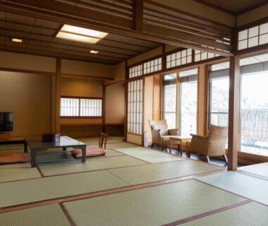 Spacious tatami room with low table, chairs by sliding doors and wooden ceiling at Izumiso in Nagano