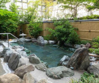 Outdoor stone onsen bath with bamboo fence and garden at Izumiso, Nagano, Chūbu, Japan