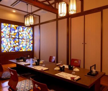 Low tatami dining room with zabuton cushions, stained glass window and wooden beams at Izumiso in Nagano