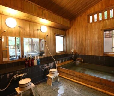 Indoor wooden onsen bath with stools, hand showers and soaking tub at Izumiya Zenbe, Nagano