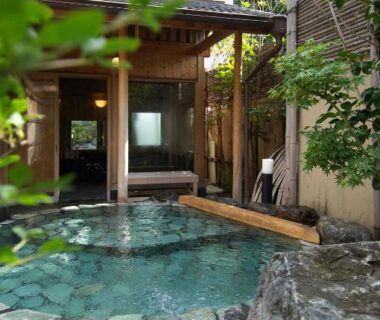 Stone-lined outdoor onsen bath with wooden shelter at Izumiya Zenbe in Nagano, Chūbu