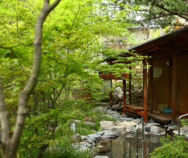 Veranda of a wooden ryokan room overlooking a lush stone garden and stream in Nagano