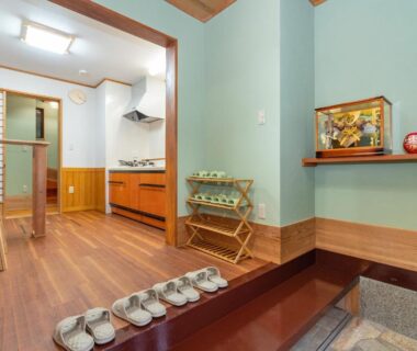 Wooden genkan with lined slippers, raised flooring, shoji screens and small kitchenette visible