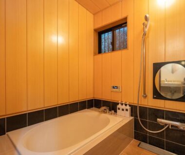 Wood-paneled bathroom with bathtub, shower, round mirror and window at Asakusa ryokan