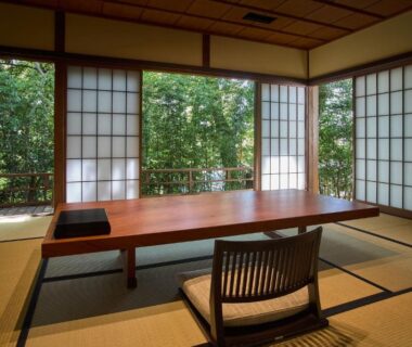 Traditional tatami room with low wooden table, zabuton chair and shoji screens overlooking a leafy garden at Jinya Ryokan, Kanagawa