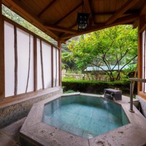 Stone soaking tub under wooden pavilion with shoji screens and garden view at Jizaiso, Kantō Tochigi