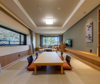 Spacious tatami room with low table, floor cushions, large windows and garden view at Jizaiso, Tochigi