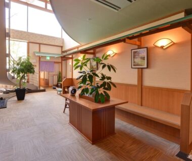 Warm wooden lobby with reception desk, potted plants, bench seating and tall windows at Jizaiso in Tochigi