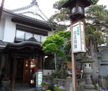 Traditional wooden ryokan entrance with stone lantern and signboard at Jizokan Matsuya in Nagano