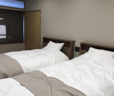 Two single beds with white duvets and beige runners in a simple ryokan room at Jizokan Matsuya in Nagano