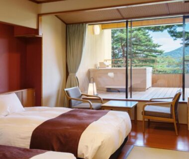 Tatami room with twin beds, low table, shoji screens and balcony opening to pine trees and distant landscape