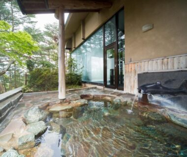 Rock-lined outdoor onsen bath beside glass doors at Jodogahama Park Hotel in Iwate