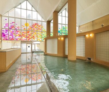 Indoor tiled onsen pool with stained glass wall and vaulted ceiling at Jozankei Tsuruga Resort Spa, Hokkaidō