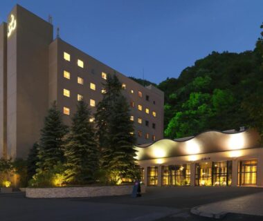 Evening exterior of multi-story resort with lit windows and entrance canopy at Jozankei Tsuruga Resort Spa Mori no Uta, Hokkaidō