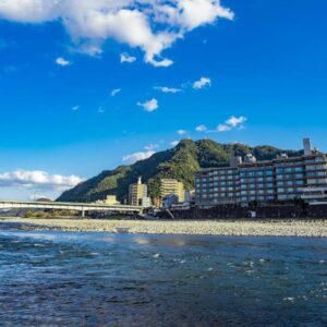 Multi-story ryokan along a riverside with bridge and mountain backdrop in Gifu, Chūbu, Japan