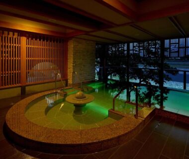 Circular indoor onsen bath with green water and wooden lattice, window overlooking river at Juhachiro, Gifu