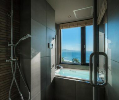 Indoor bath and shower with large window framing coastal sea view and distant coastline at Jukaitei, Kyoto