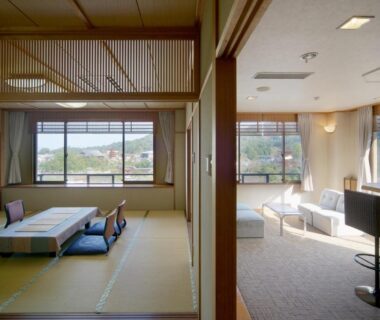 Tatami room with low table and floor cushions beside a bright lounge with large windows at Jukeiso, Hiroshima