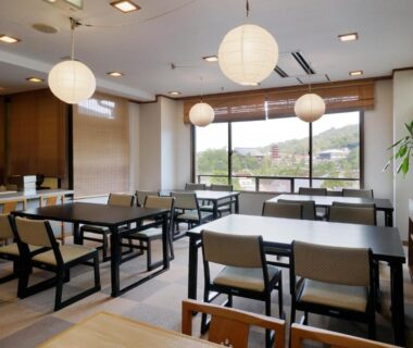 Spacious ryokan dining with paper lanterns, tables and chairs and large windows overlooking green landscape