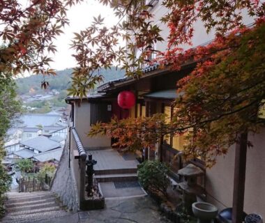 Stone steps lined with maple trees leading to Jukeiso entrance overlooking a Hiroshima hillside town
