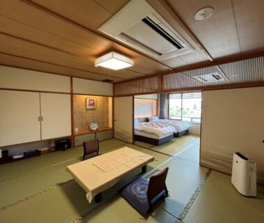 Tatami room with low table, zaisu chairs, two Western beds and large window overlooking greenery