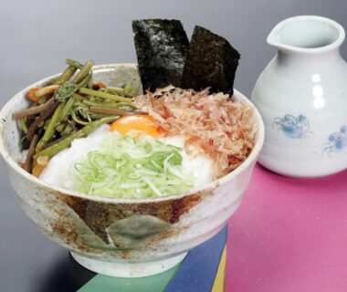 Ceramic bowl topped with seaweed, scallions, mountain vegetables and bonito flakes beside a small ceramic pourer