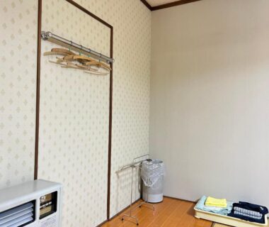 Folded futon and hanger rack beside heater in Juvankan guest room, Nagano, Chūbu, Japan